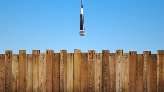 A microphone dangles over a wooden fence.