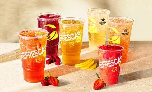 Several plastic cups filled with ice and red, orange, and yellow sodas. The cups read, 'Taco Bell Refrescas.'