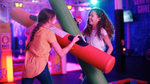 Two young girls laugh as they play with large foam 'battle beams'