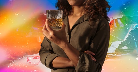 A woman holds a rocks glass with whiskey in it.