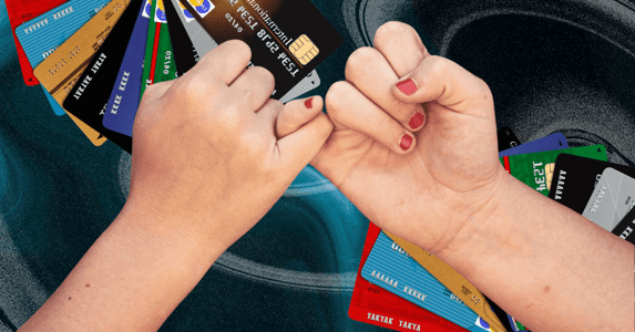 Two white hands with nail polish on in a pinky swear with credit cards in the background. 