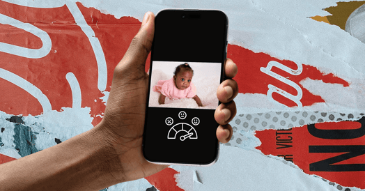 A Black arm holding a smartphone showing a Black baby crawling with a happiness scale underneath.