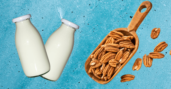 Two bottles of milk and a scoop of pecans on a blue background.